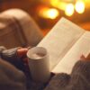 woman reading a book with a hot coco on a warm cozy environment