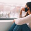 woman with face mask looking outside the window on winter