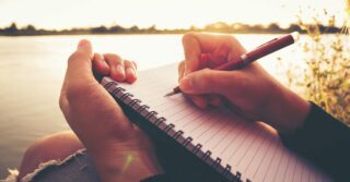 close up hand of young woman with pen writing a journal